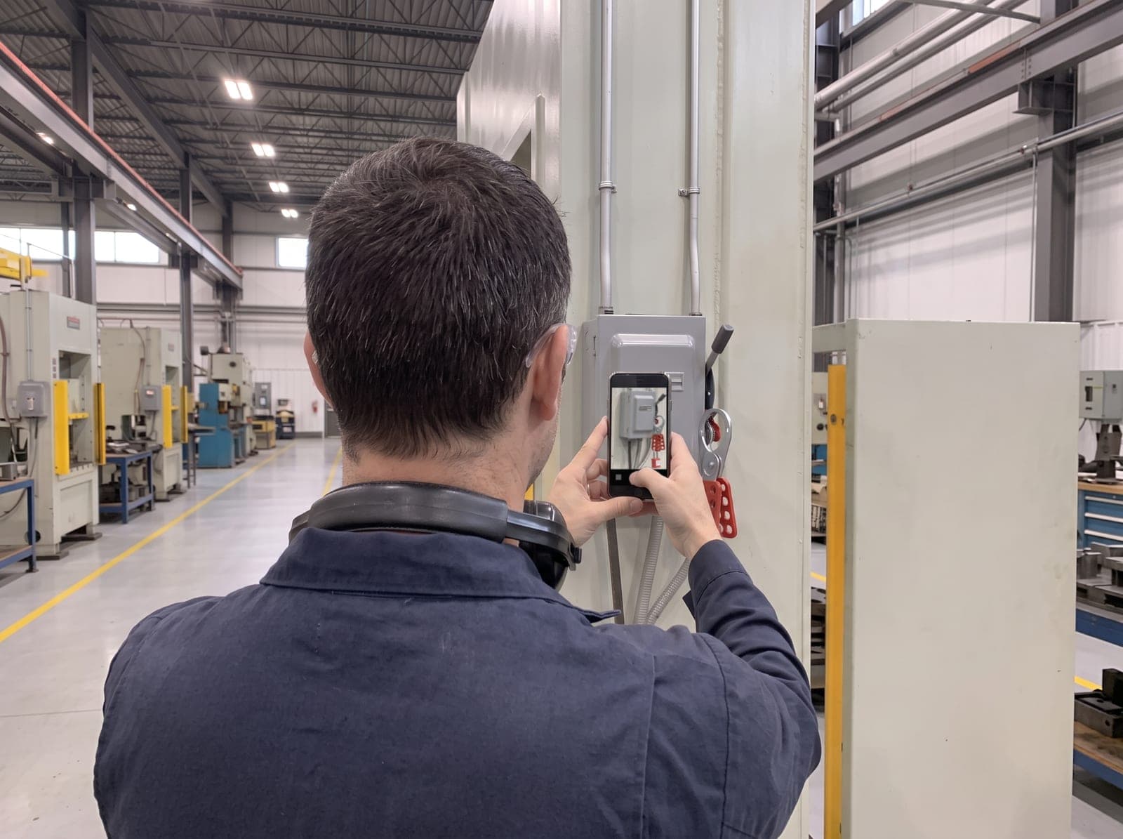 Technician photographing a locked-out disconnect switch with a phone, on the plant floor